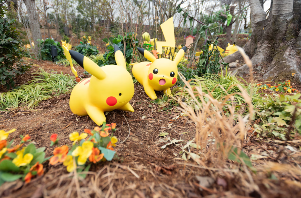 Two yellow Pikachu figurines walking in a garden filled with flowers and greenery.